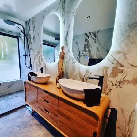 Finished bathroom with marble walls, a timber vanity and twin basins